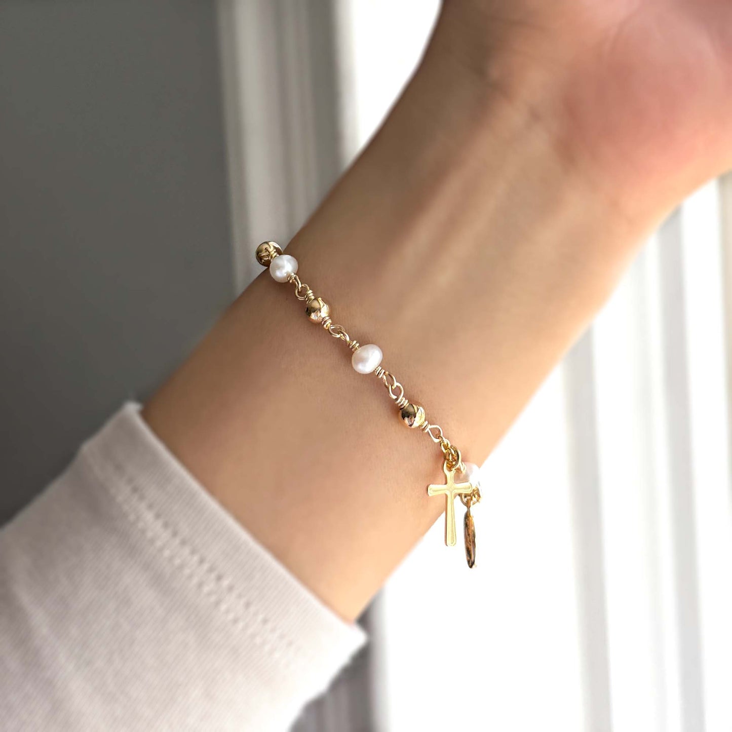 A person wearing a gold-filled Saint Benedict rosary bracelet with freshwater pearls and gold-filled charms on their wrist.