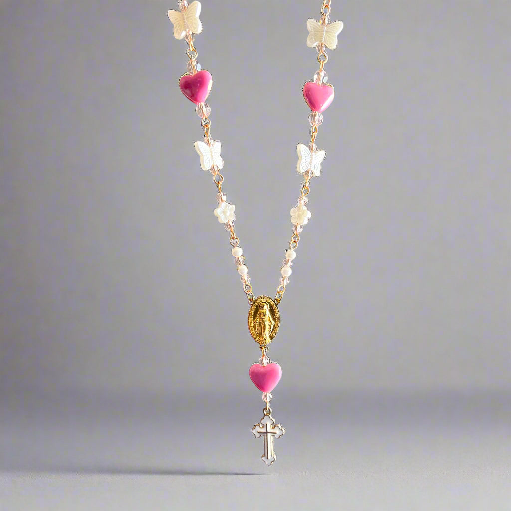 Necklace with pink heart beads, white flowers, and a cross pendant on a gray background