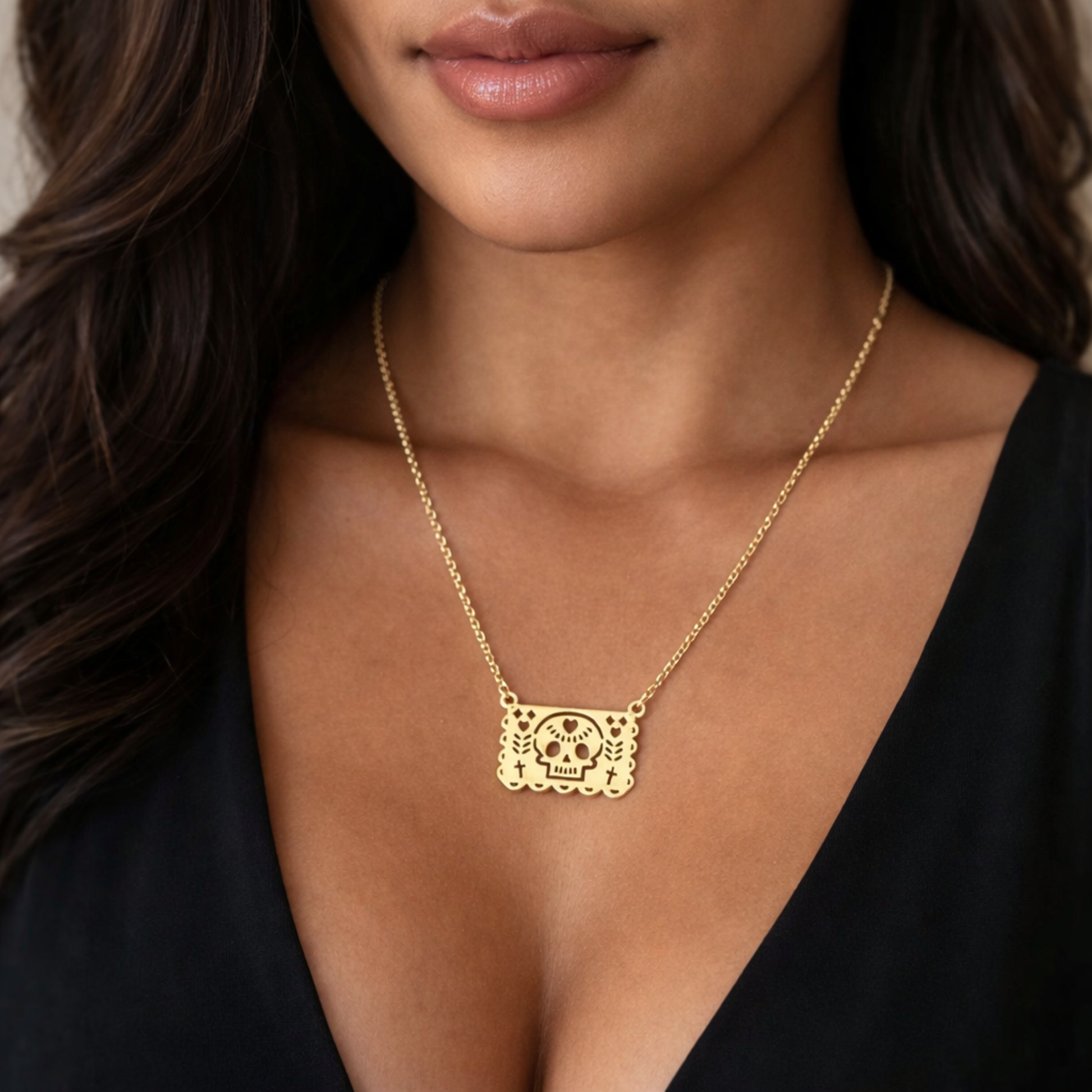 Gold necklace with a skull pendant worn by a person against a neutral background
