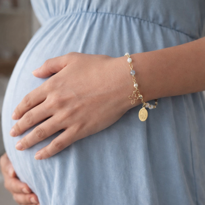 Pregnant person wearing a gold bracelet with charms on a light blue dress.