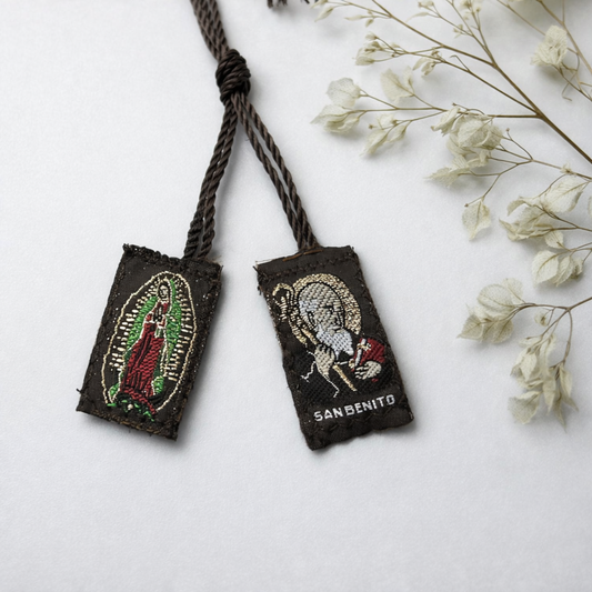 Two embroidered pouches with Virgin Mary and Saint Benedict designs on a white surface with dried flowers.