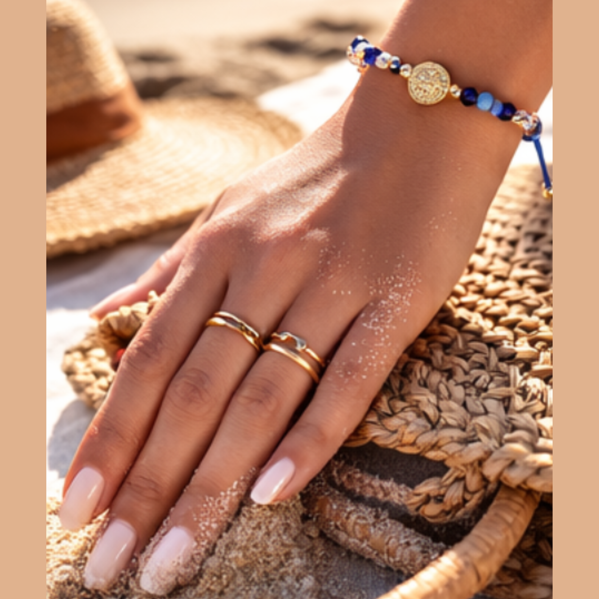 Hand with gold rings and a beaded bracelet on a woven surface
