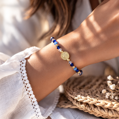 Close-up of a wrist wearing a beaded bracelet with a decorative gold charm, blurred background