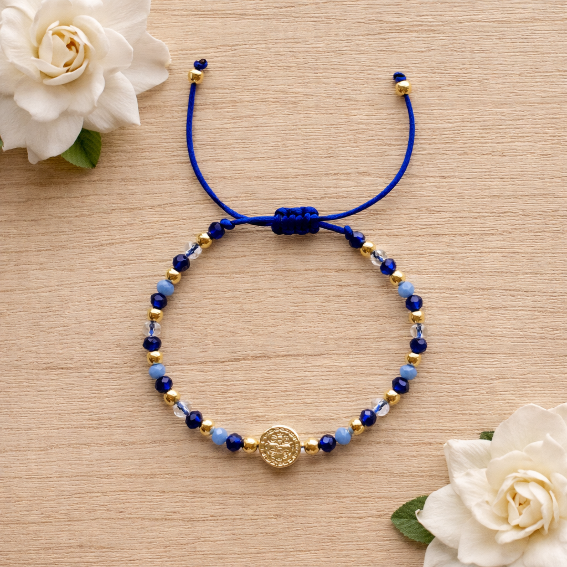 Blue beaded bracelet with a gold charm on a wooden surface with white flowers.