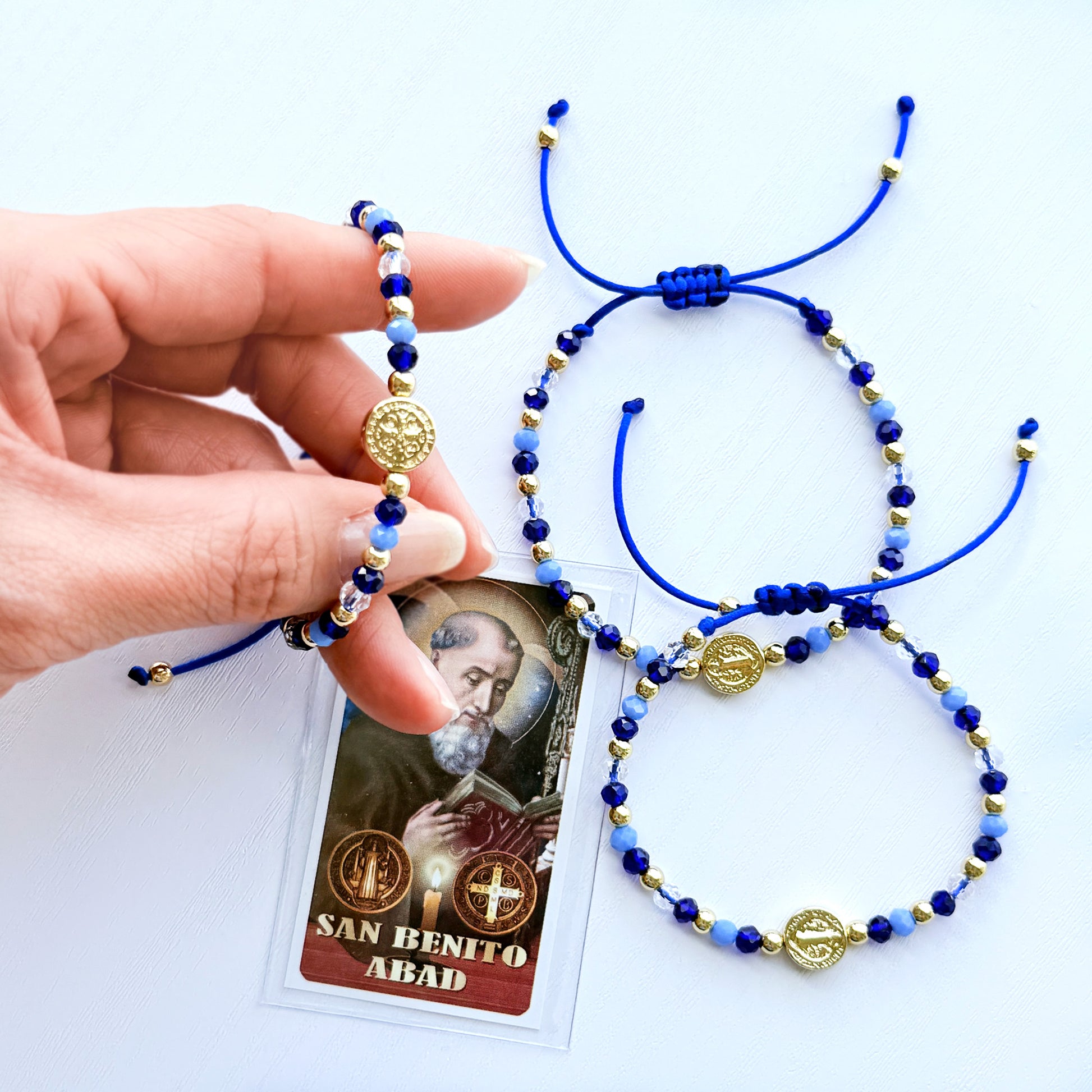 Blue and gold beaded bracelet with a card featuring 'San Benito Abad' on a white background