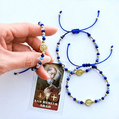 Blue and gold beaded bracelet with a card featuring 'San Benito Abad' on a white background
