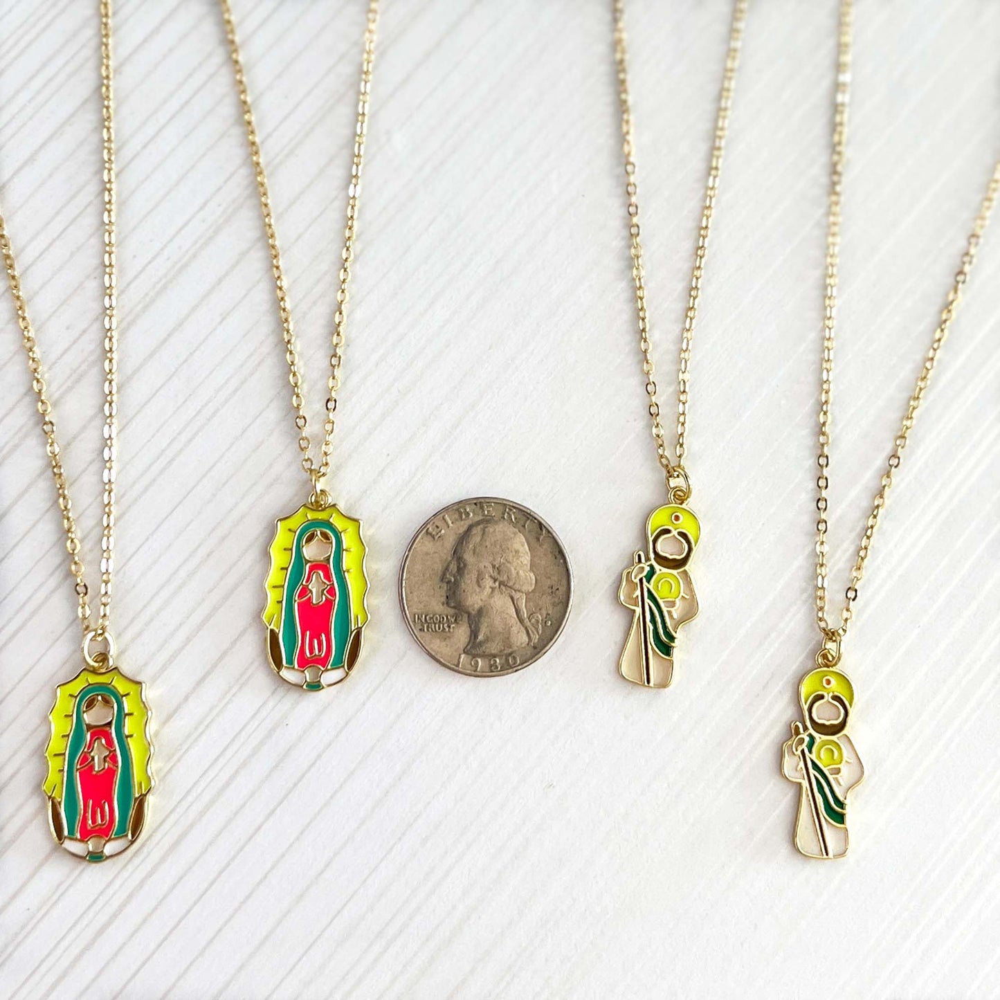 Two gold necklaces with Virgin Mary pendants on a white background, one with a quarter for scale.