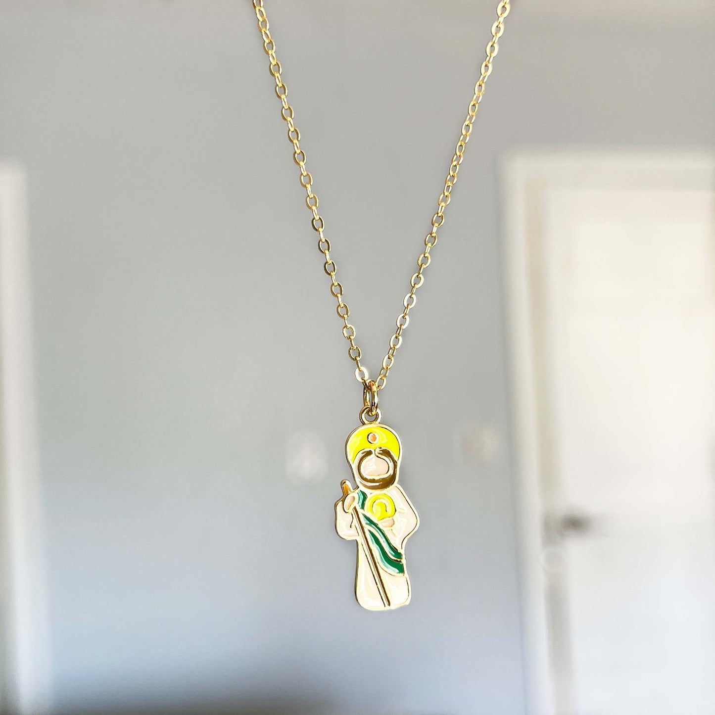 Gold necklace with a pendant of a Saint Jude a yellow flower on a neutral background