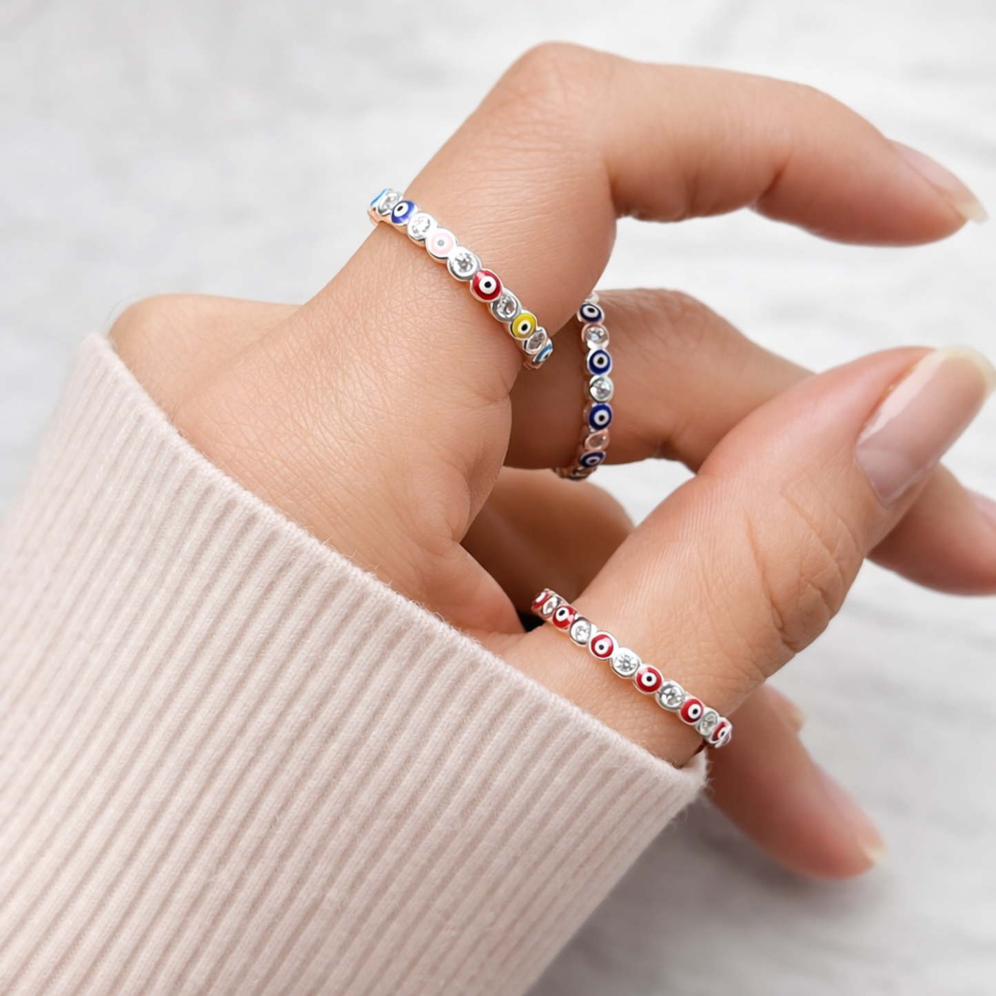 Hand wearing two colorful evil eye rings on a light background
