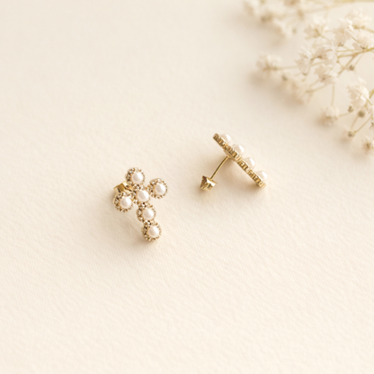 Gold cross-shaped earrings on a light beige background with dried flowers.