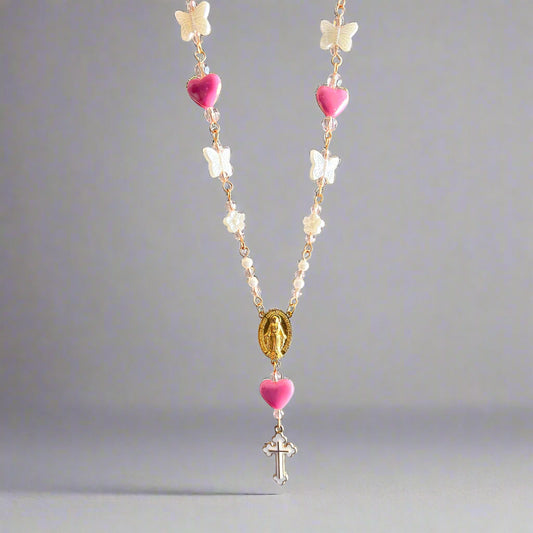 Necklace with pink heart beads, white flowers, and a cross pendant on a gray background