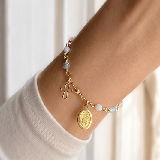 Gold bracelet with religious charms on a wrist against a neutral background