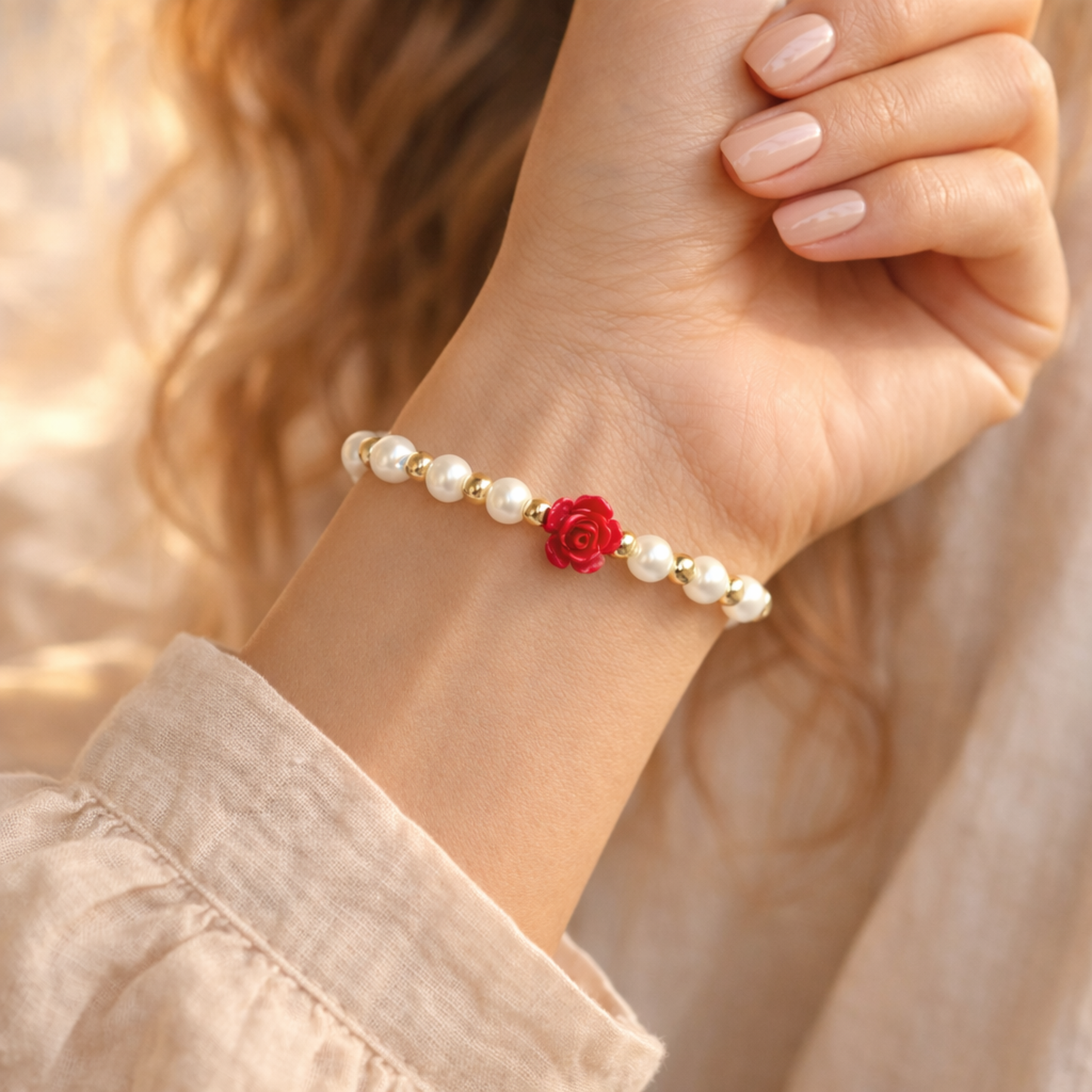 Hand wearing a pearl bracelet with a red flower charm against a blurred background