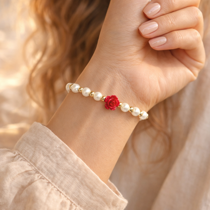 Hand wearing a pearl bracelet with a red flower charm against a blurred background