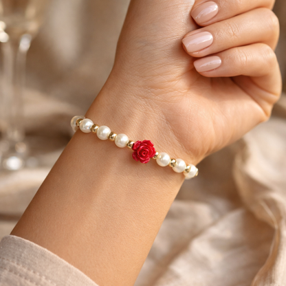 Pearl bracelet with a red flower charm on a wrist, blurred background