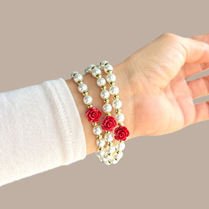 Hand wearing a pearl bracelet with red rose charms on a beige background